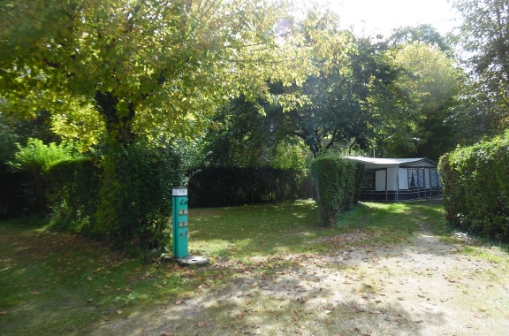 Emplacement camping délimité par des haies et disposant d’une borne électrique